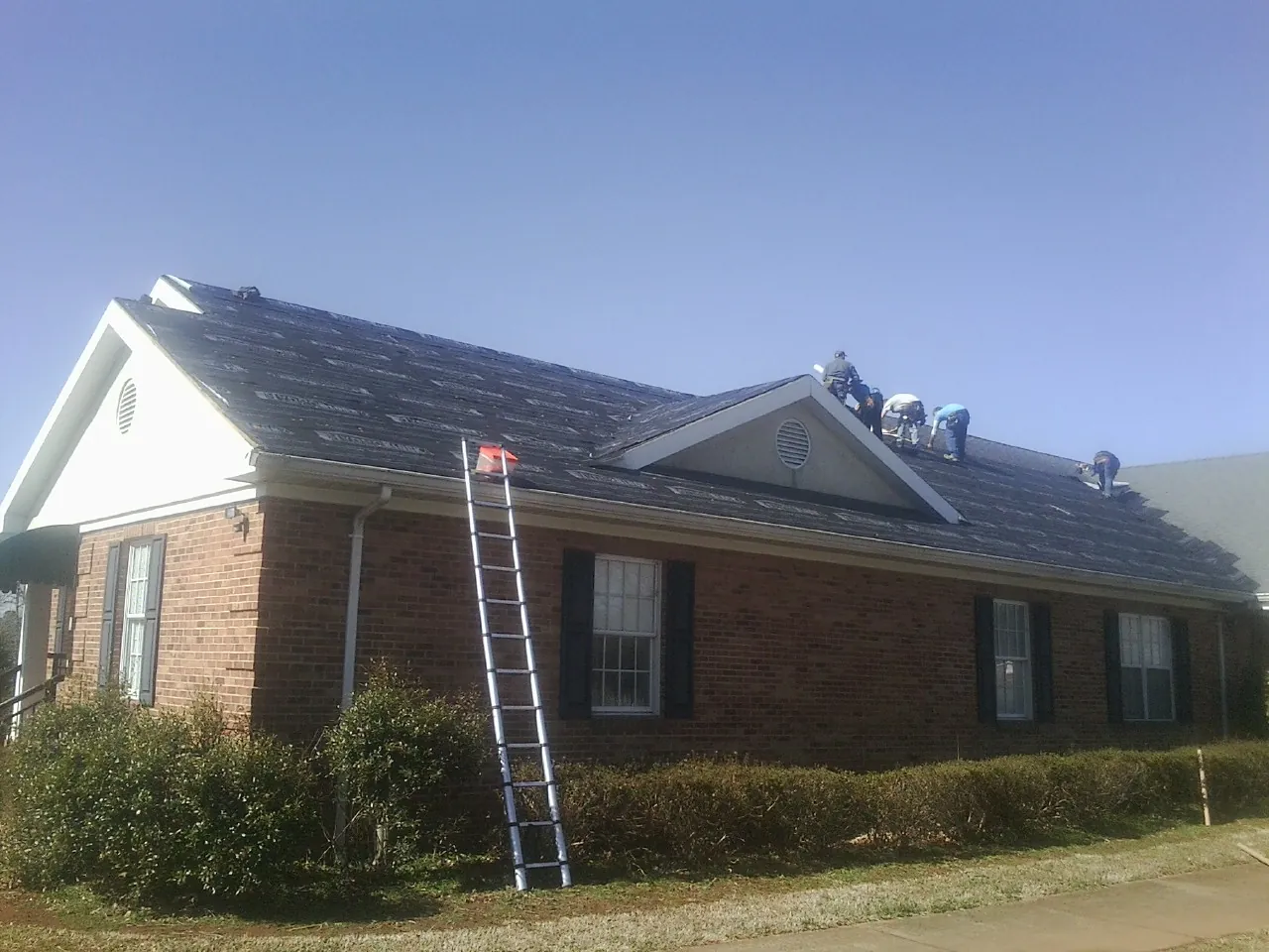Crew tearing shingles off a brick ranch roof with a ladder set — Emergency Roof Repair work by our crew in Van