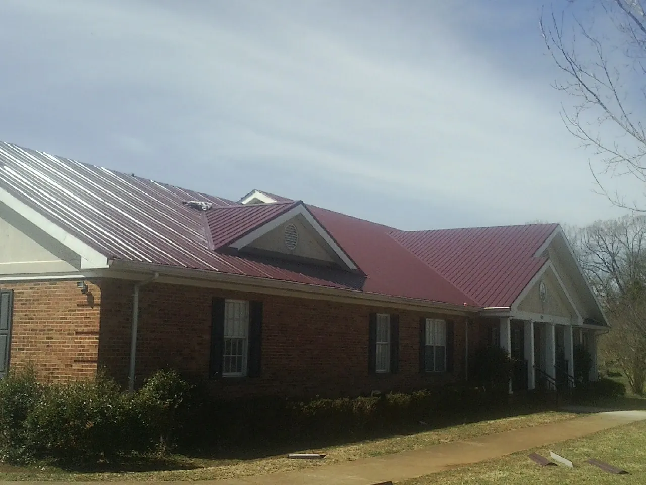 Red metal roof with gabled entries on a long brick building, from a Hail Damage Roof Repair job in Van